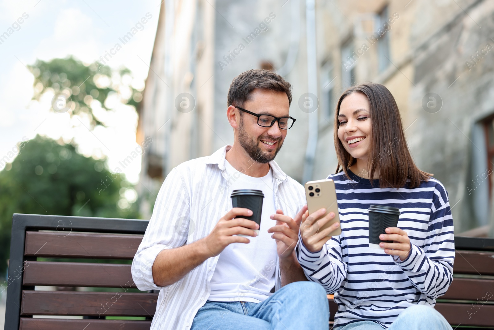 Photo of Coffee to go. Couple with paper cups of drinks and smartphone on bench outdoors