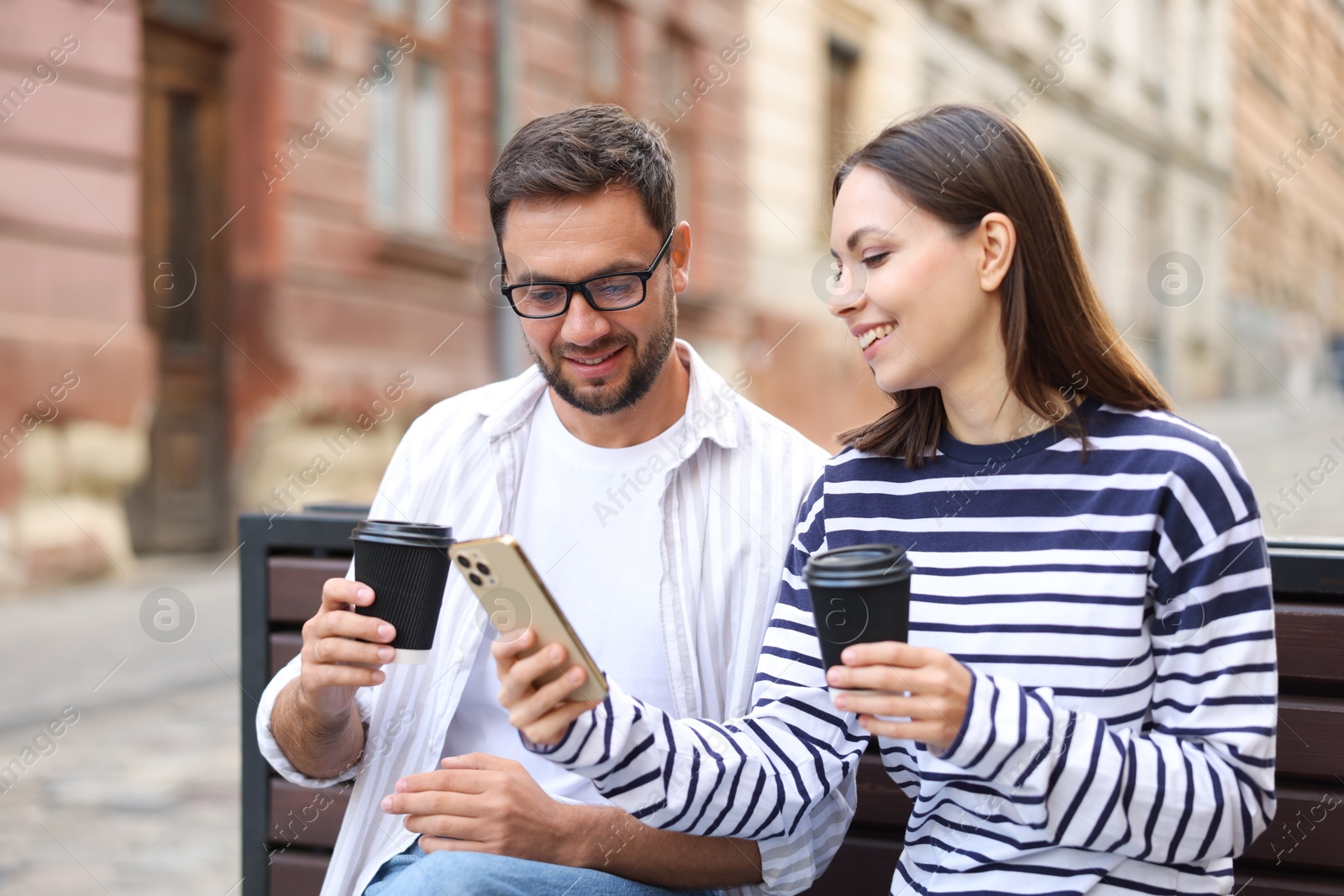 Photo of Coffee to go. Couple with paper cups of drinks and smartphone on bench outdoors