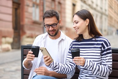 Photo of Coffee to go. Couple with paper cups of drinks and smartphone on bench outdoors