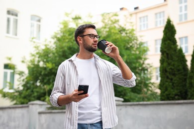 Photo of Coffee to go. Man with paper cup of drink and smartphone outdoors