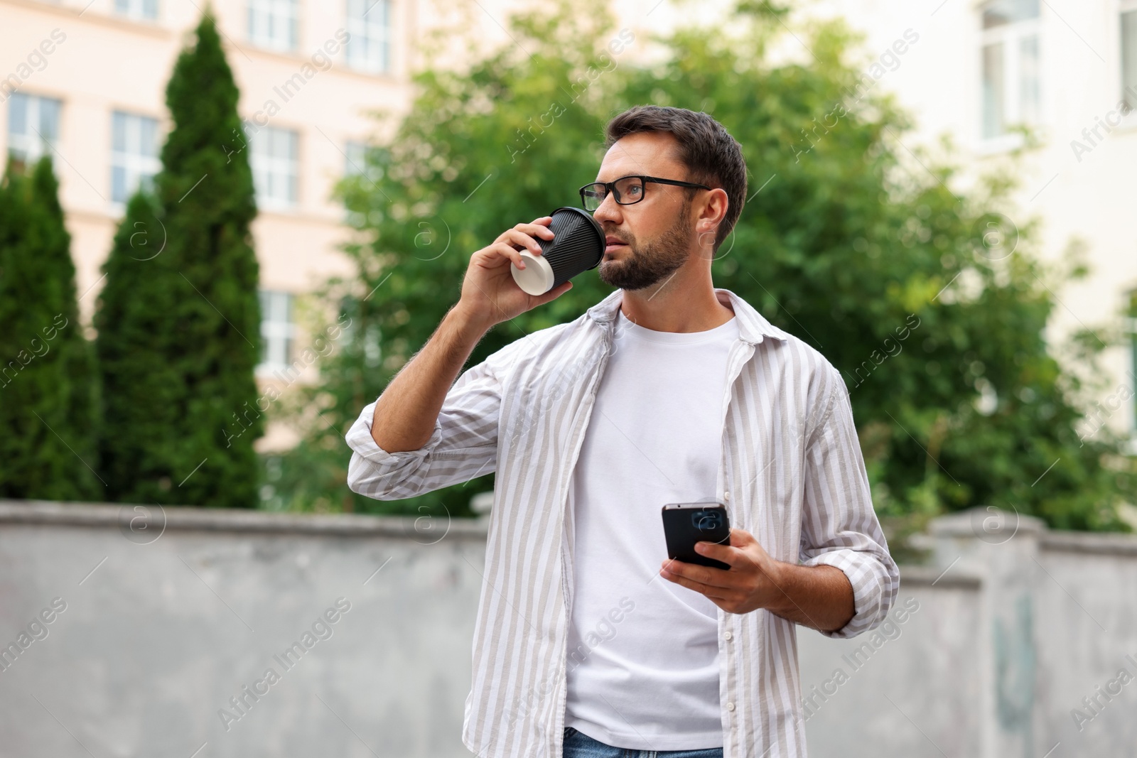 Photo of Coffee to go. Man with paper cup of drink and smartphone outdoors