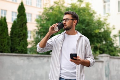 Photo of Coffee to go. Man with paper cup of drink and smartphone outdoors
