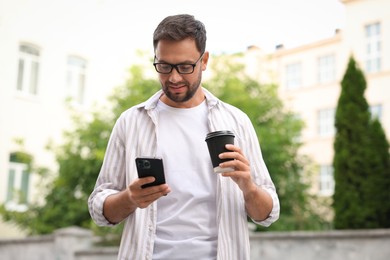 Photo of Coffee to go. Man with paper cup of drink and smartphone outdoors