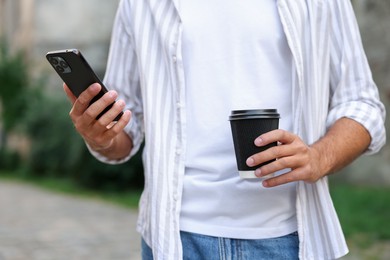 Photo of Coffee to go. Man with paper cup of drink and smartphone outdoors, closeup