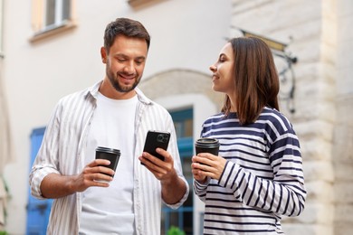 Photo of Coffee to go. Couple with paper cups of drinks and smartphone on city street