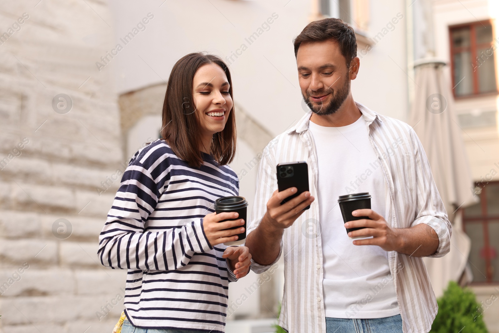Photo of Coffee to go. Couple with paper cups of drinks and smartphone on city street