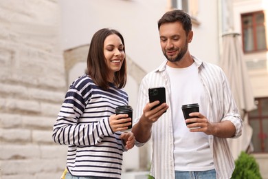 Photo of Coffee to go. Couple with paper cups of drinks and smartphone on city street