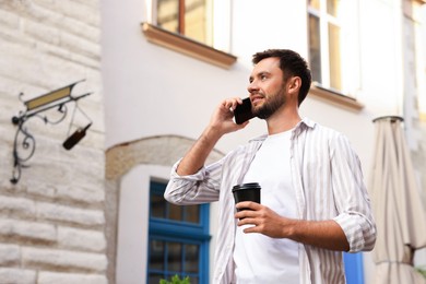 Photo of Coffee to go. Man with paper cup of drink talking on smartphone outdoors, low angle view. Space for text