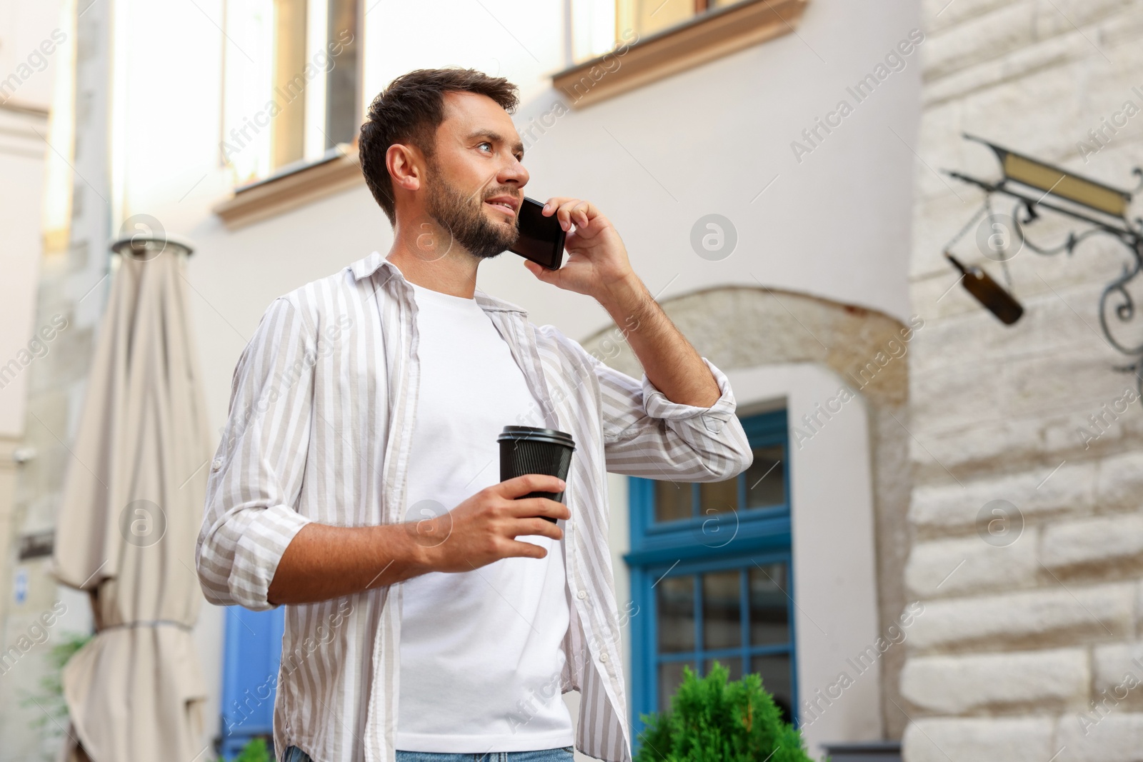 Photo of Coffee to go. Man with paper cup of drink talking on smartphone outdoors, low angle view. Space for text