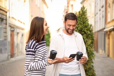 Photo of Coffee to go. Couple with paper cups of drinks and smartphone outdoors