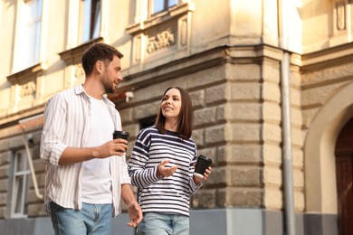 Photo of Coffee to go. Couple with paper cups of drinks walking on city street, low angle view. Space for text