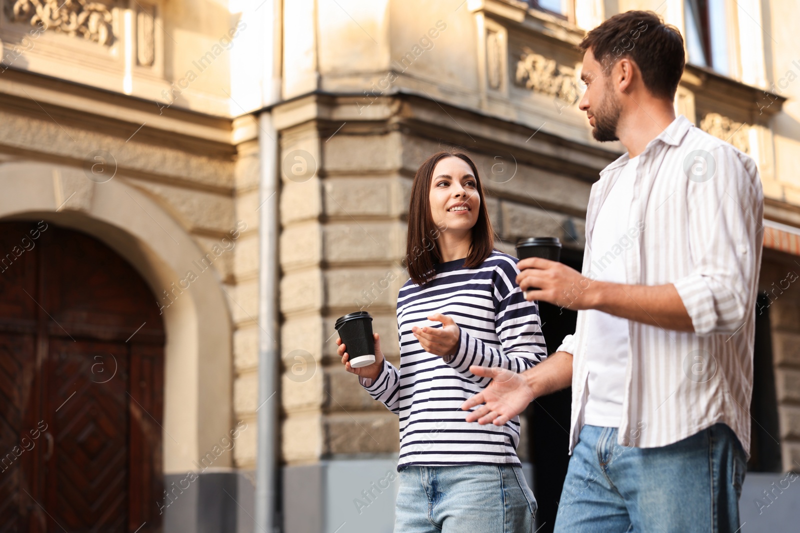 Photo of Coffee to go. Couple with paper cups of drinks walking on city street, low angle view. Space for text
