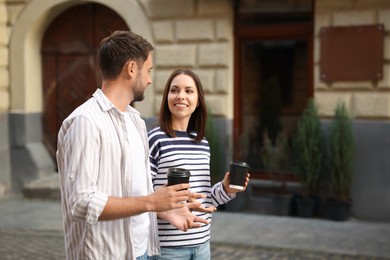 Photo of Coffee to go. Couple with paper cups of drinks walking on city street, space for text