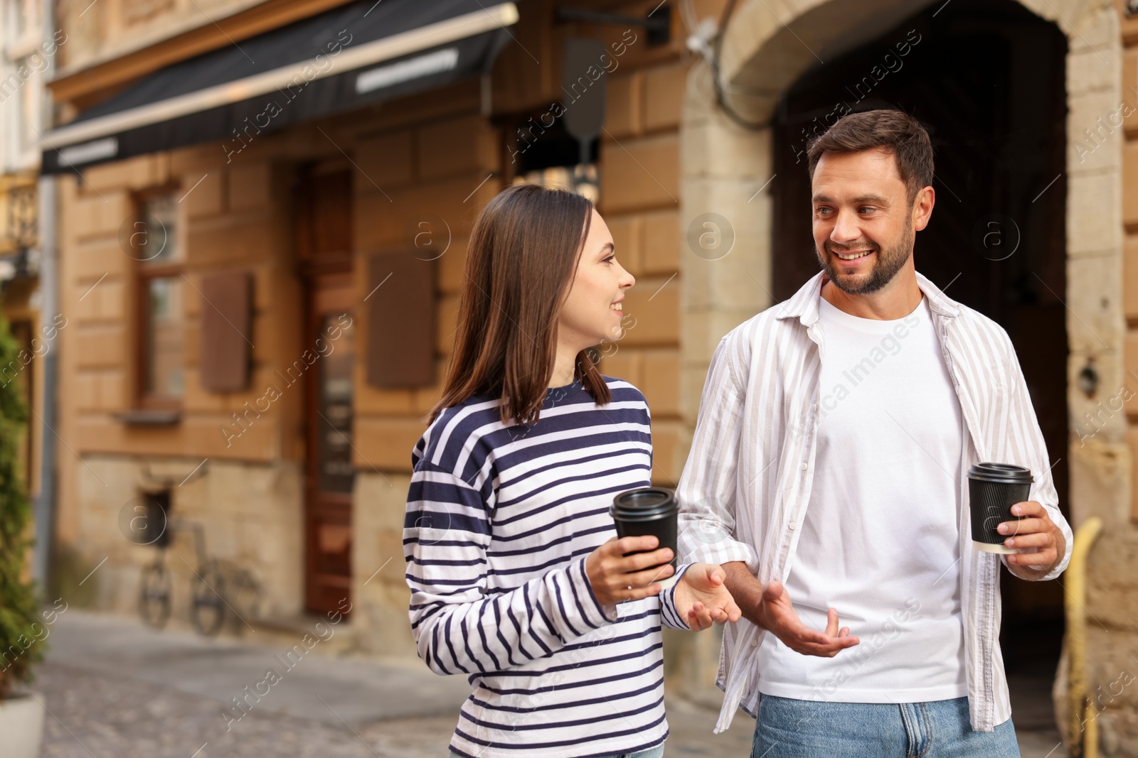 Photo of Coffee to go. Couple with paper cups of drinks walking on city street, space for text
