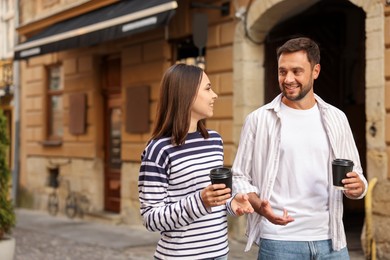 Photo of Coffee to go. Couple with paper cups of drinks walking on city street, space for text
