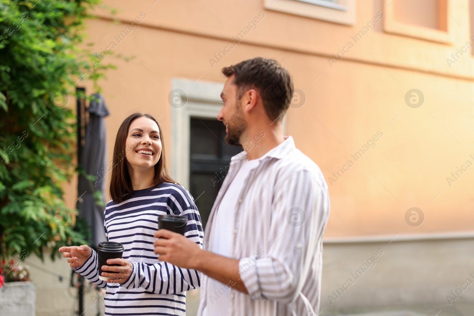 Photo of Coffee to go. Couple with paper cups of drinks walking on city street, space for text