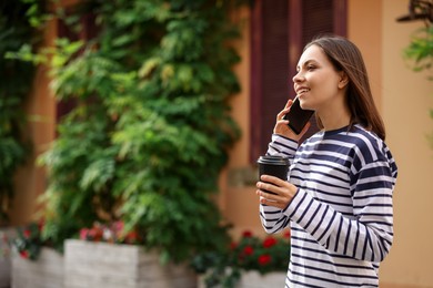 Photo of Coffee to go. Woman with paper cup of drink talking on smartphone outdoors, space for text