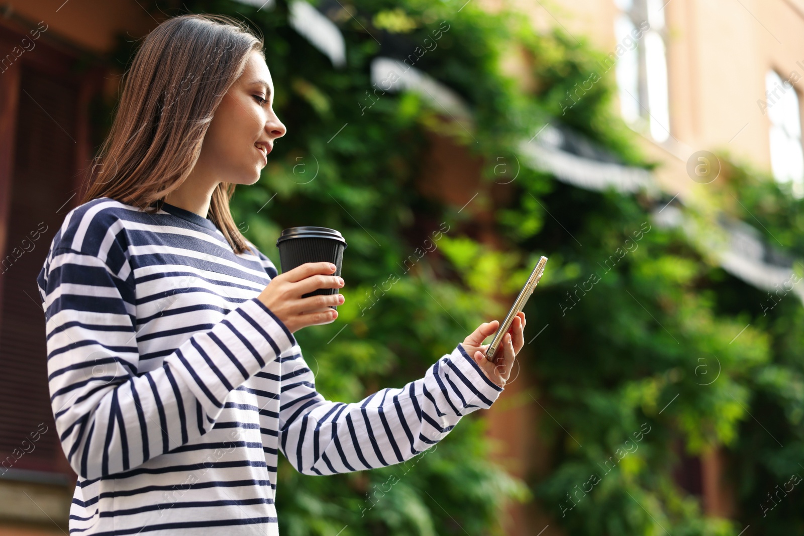 Coffee to go. Woman with paper cup of drink and smartphone outdoors, low angle view. Space for text Photo of Coffee to go. Woman with paper cup of drink and smartphone outdoors, low angle view. Space for text