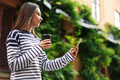 Photo of Coffee to go. Woman with paper cup of drink and smartphone outdoors, low angle view. Space for text