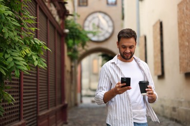 Photo of Coffee to go. Man with paper cup of drink and smartphone outdoors, space for text
