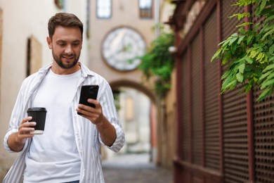 Photo of Coffee to go. Man with paper cup of drink and smartphone outdoors, space for text