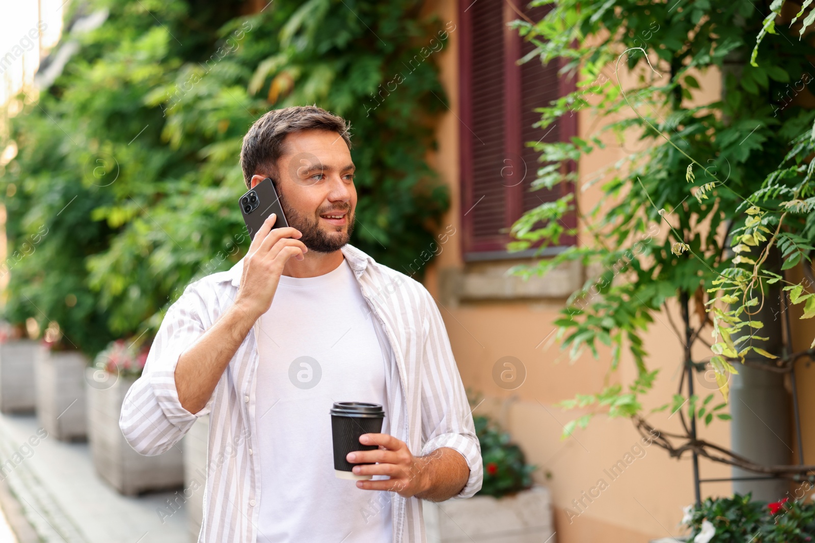 Photo of Coffee to go. Man with paper cup of drink talking on smartphone outdoors