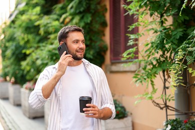 Photo of Coffee to go. Man with paper cup of drink talking on smartphone outdoors
