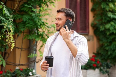 Photo of Coffee to go. Man with paper cup of drink talking on smartphone outdoors