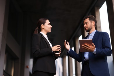 Photo of Coffee to go. Woman with paper cup of drink and her business partner during meeting outdoors, low angle view