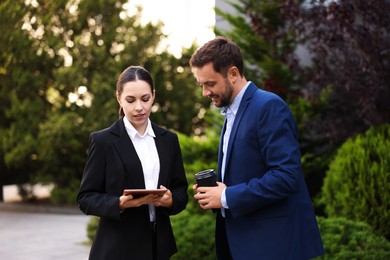Photo of Coffee to go. Man with paper cup of drink and his business partner during meeting outdoors