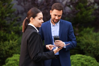 Photo of Coffee to go. Man with paper cup of drink and his business partner during meeting outdoors