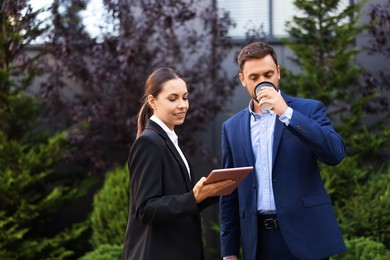 Photo of Coffee to go. Man with paper cup of drink and his business partner during meeting outdoors, space for text