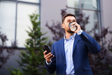Photo of Coffee to go. Man with paper cup of drink and smartphone outdoors, low angle view. Space for text