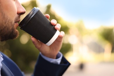 Photo of Coffee to go. Man with paper cup of drink outdoors, closeup. Space for text