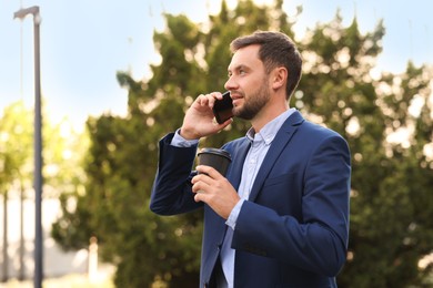 Photo of Coffee to go. Man with paper cup of drink talking on smartphone outdoors, space for text