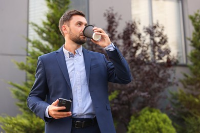 Photo of Coffee to go. Man with paper cup of drink and smartphone outdoors, low angle view. Space for text