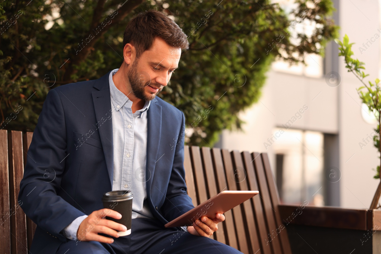 Photo of Coffee to go. Man with paper cup of drink and tablet on bench outdoors