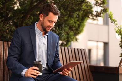 Photo of Coffee to go. Man with paper cup of drink and tablet on bench outdoors