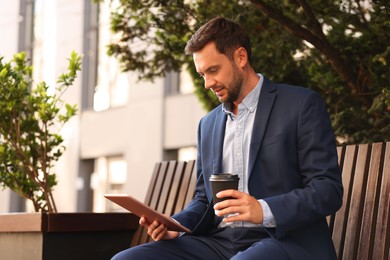 Photo of Coffee to go. Man with paper cup of drink and tablet on bench outdoors