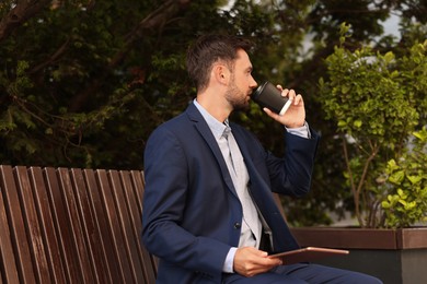 Photo of Coffee to go. Man with paper cup of drink and tablet on bench outdoors