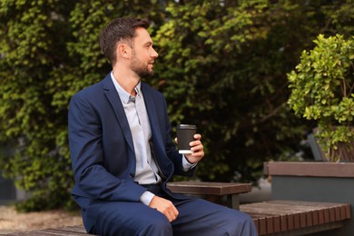 Photo of Coffee to go. Man with paper cup of drink on bench outdoors, space for text
