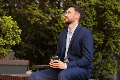 Photo of Coffee to go. Man with paper cup of drink on bench outdoors, space for text