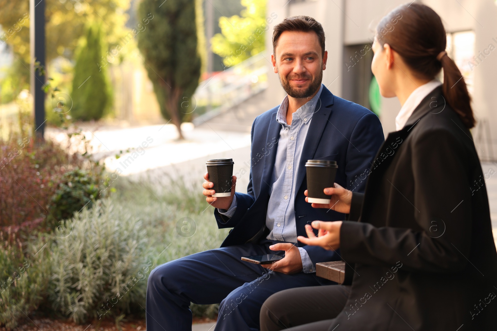 Photo of Coffee to go. Businesspeople with paper cups of drinks on bench outdoors, space for text