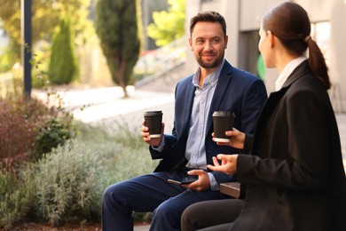 Photo of Coffee to go. Businesspeople with paper cups of drinks on bench outdoors, space for text