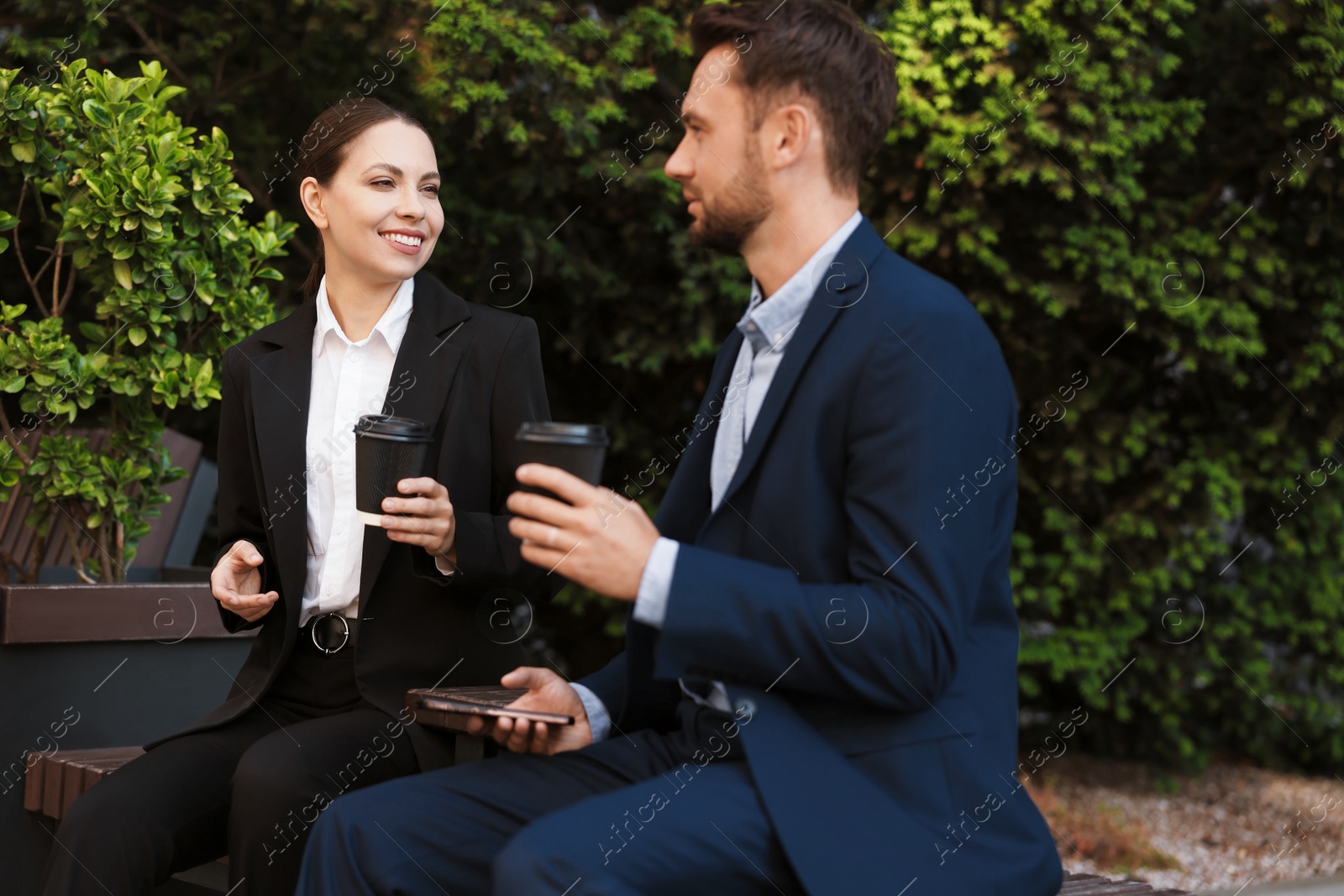 Photo of Coffee to go. Businesspeople with paper cups of drinks on bench outdoors