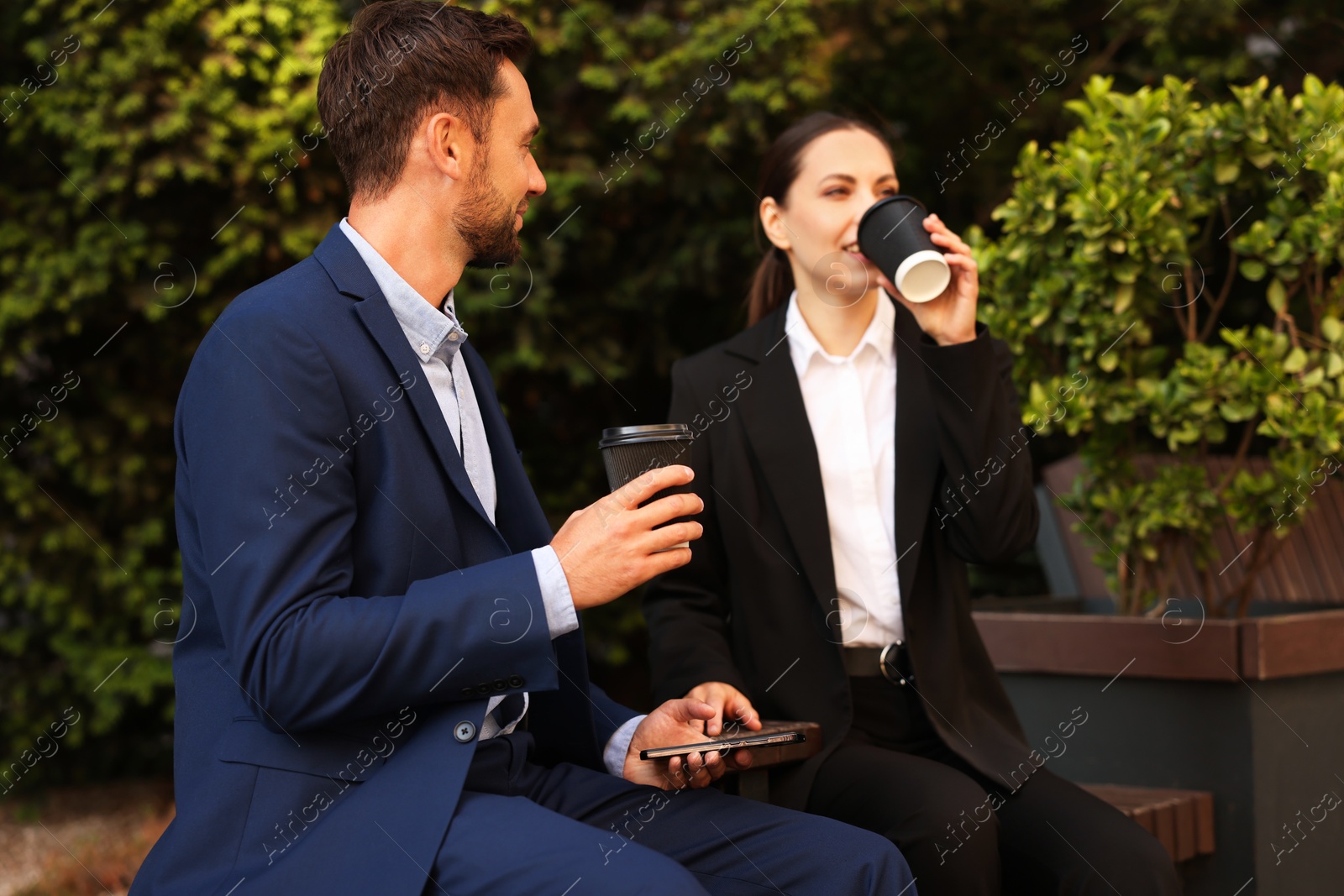 Photo of Coffee to go. Businesspeople with paper cups of drinks on bench outdoors