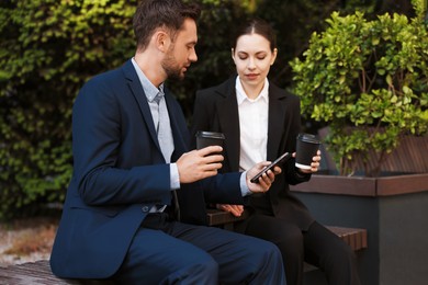 Photo of Coffee to go. Businesspeople with paper cups of drinks on bench outdoors