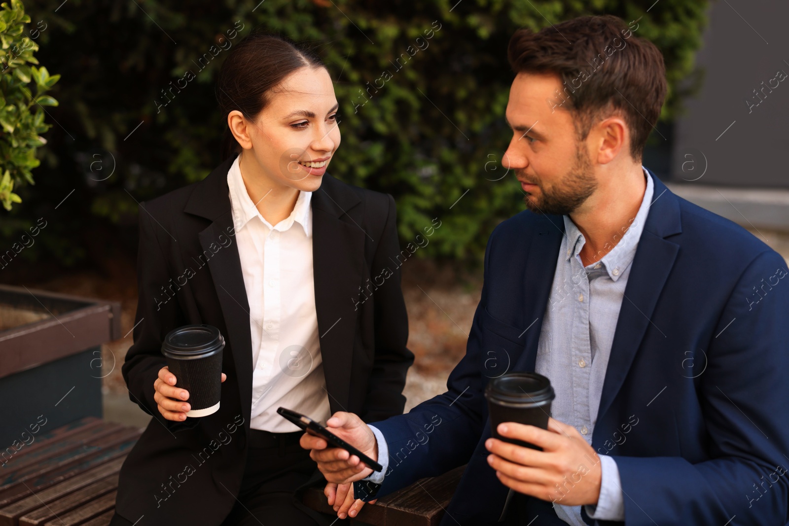 Photo of Coffee to go. Businesspeople with paper cups of drinks on bench outdoors