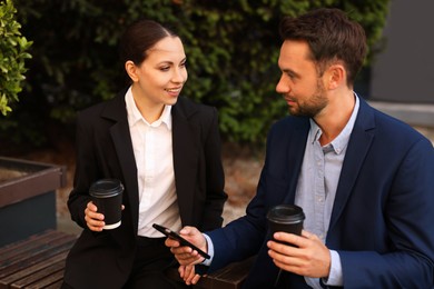 Photo of Coffee to go. Businesspeople with paper cups of drinks on bench outdoors