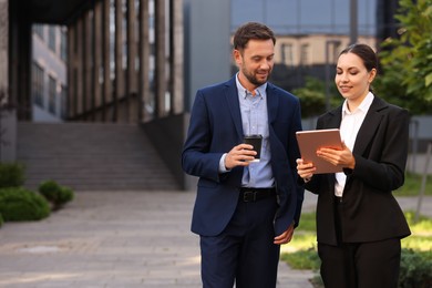 Photo of Coffee to go. Man with paper cup of drink and his business partner during meeting outdoors, space for text
